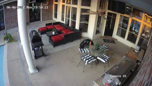 Patio with red and black seating, a round table, grill, and windows along the wall