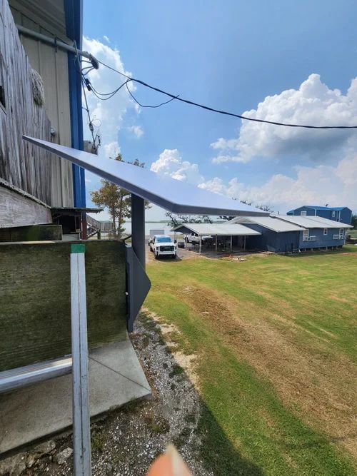 Solar panel mounted beside a barn, overlooking a grassy yard with buildings and a white truck.
