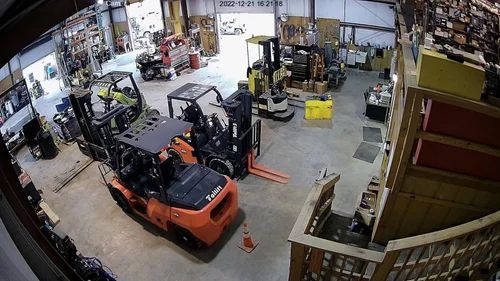 Indoor warehouse with several forklifts parked around an open floor and shelving.