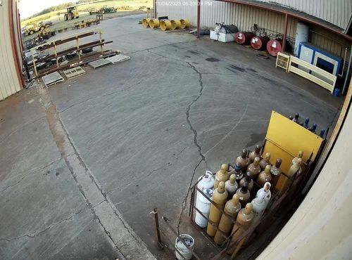 Wide-angle view of an empty warehouse yard with gas cylinders, pallets, and a large cracked concrete floor