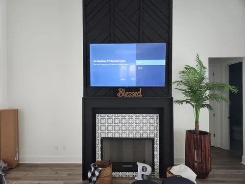 Living room with a TV above a black fireplace, potted plant, and woven decor baskets