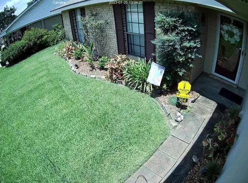 Front yard with green lawn, brick house, garden beds, and a yellow fire hydrant near the walkway.