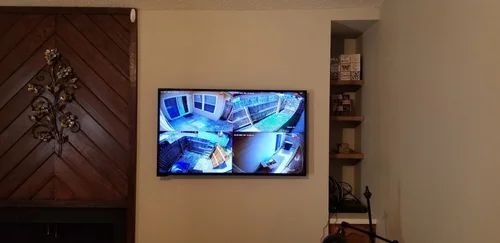 Wall-mounted TV showing a security camera view in a hallway beside a decorative wooden door