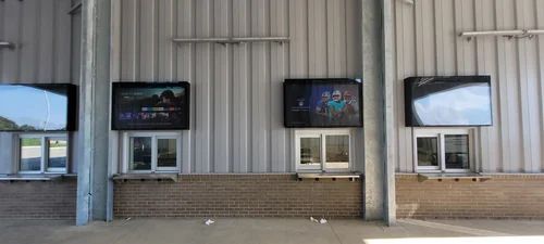 Outdoor building facade with three wall-mounted screens above windows and a brick base.