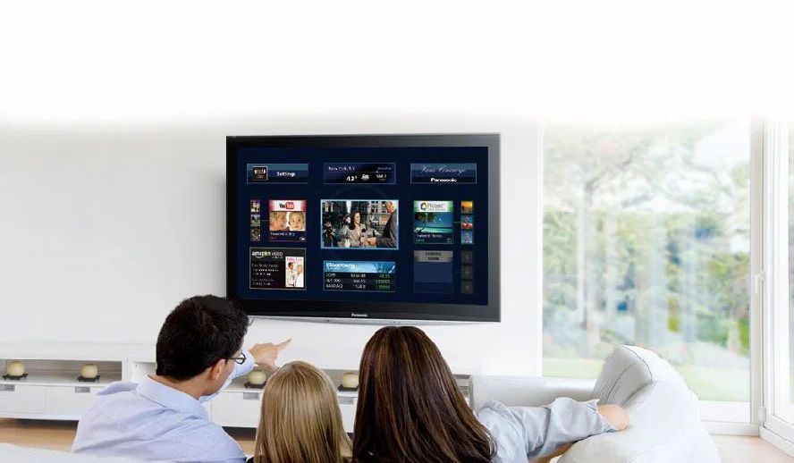 People sitting on a couch watching a wall-mounted TV in a bright living room