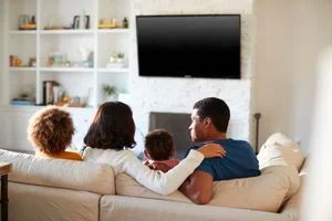 Family sitting on a beige couch watching a blank TV in a bright living room