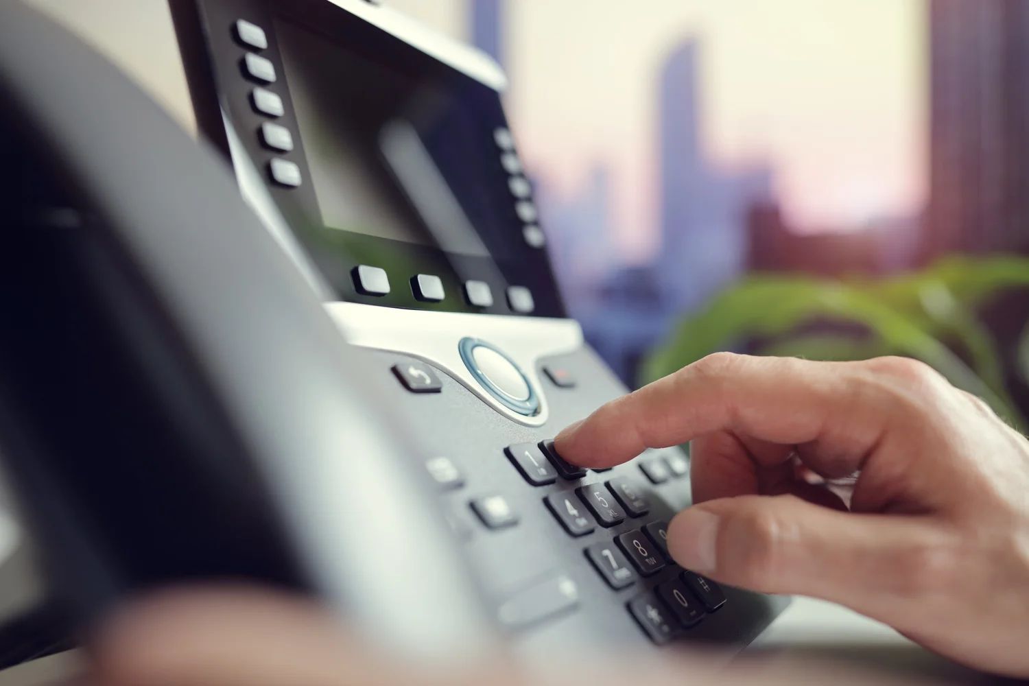 Hand pressing a desk phone keypad in an office setting