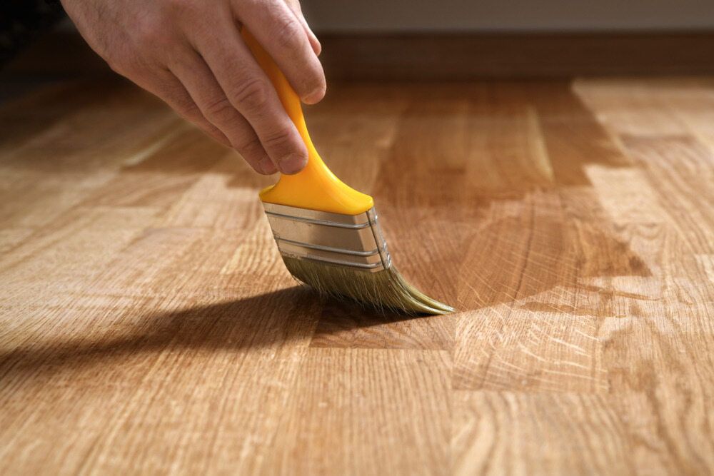 A Person is Painting a Wooden Floor With a Roller  — NHM Painting & Projects in Ciccone, NT