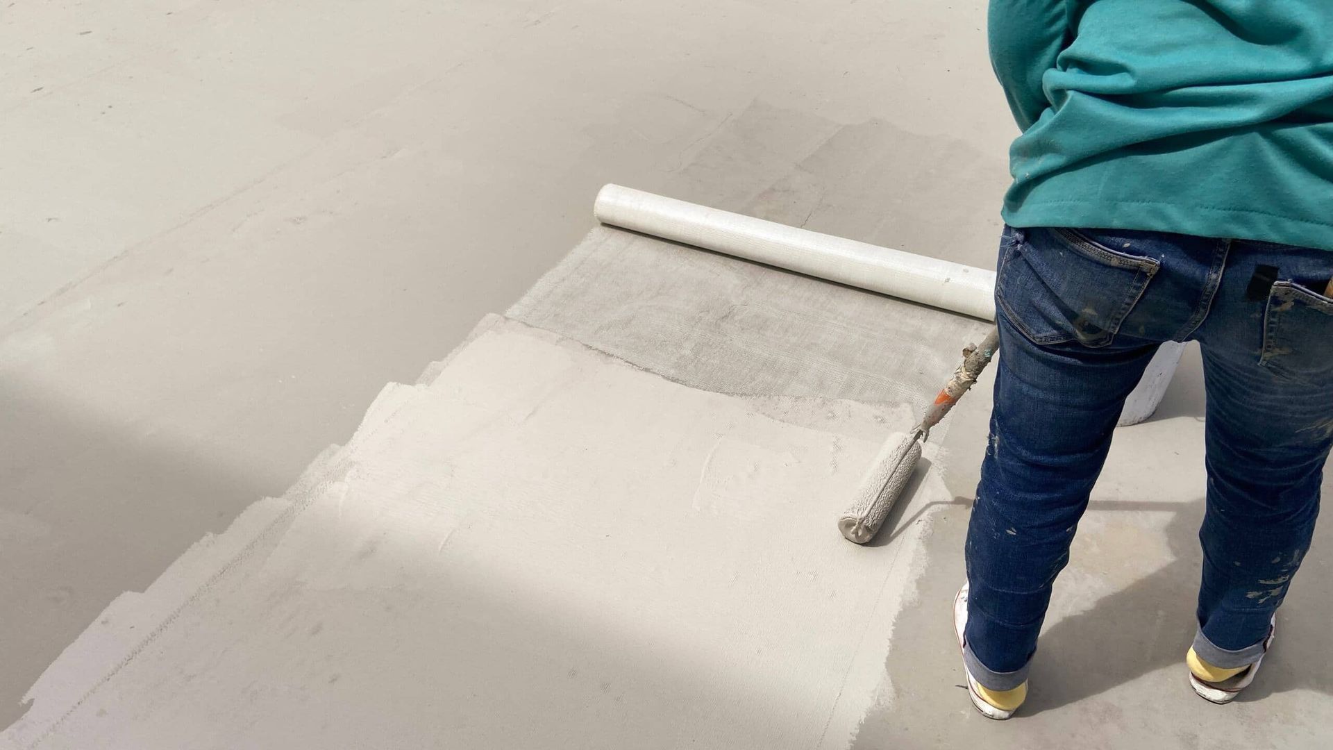 A Person is Painting a Concrete Floor With a Paint Roller  — NHM Painting & Projects in Ciccone, NT