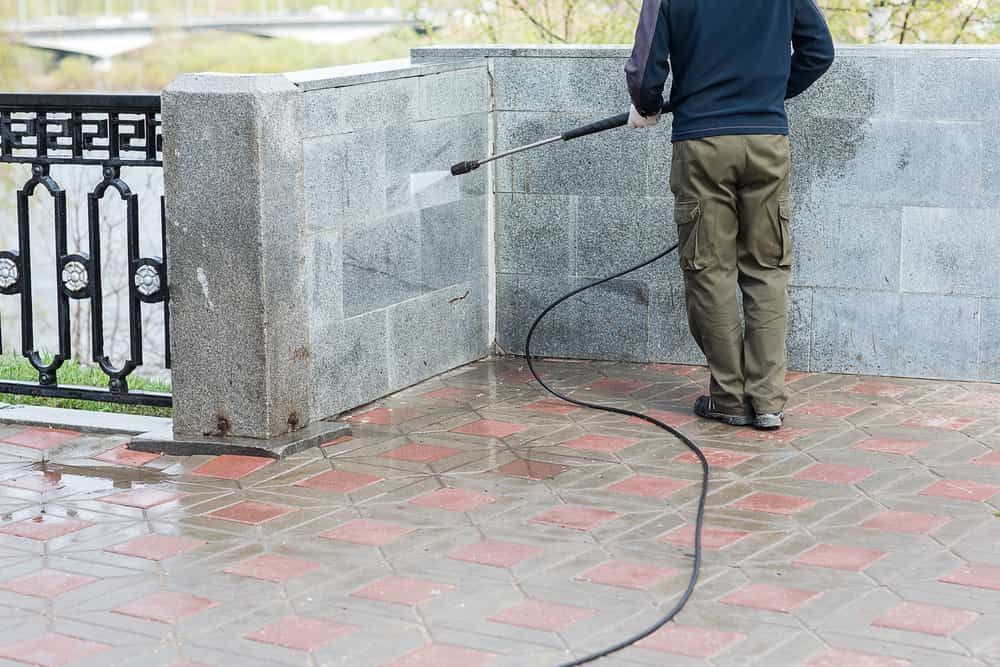 A Man is Cleaning a Brick Wall With a High Pressure Washer — NHM Painting & Projects in Ciccone, NT