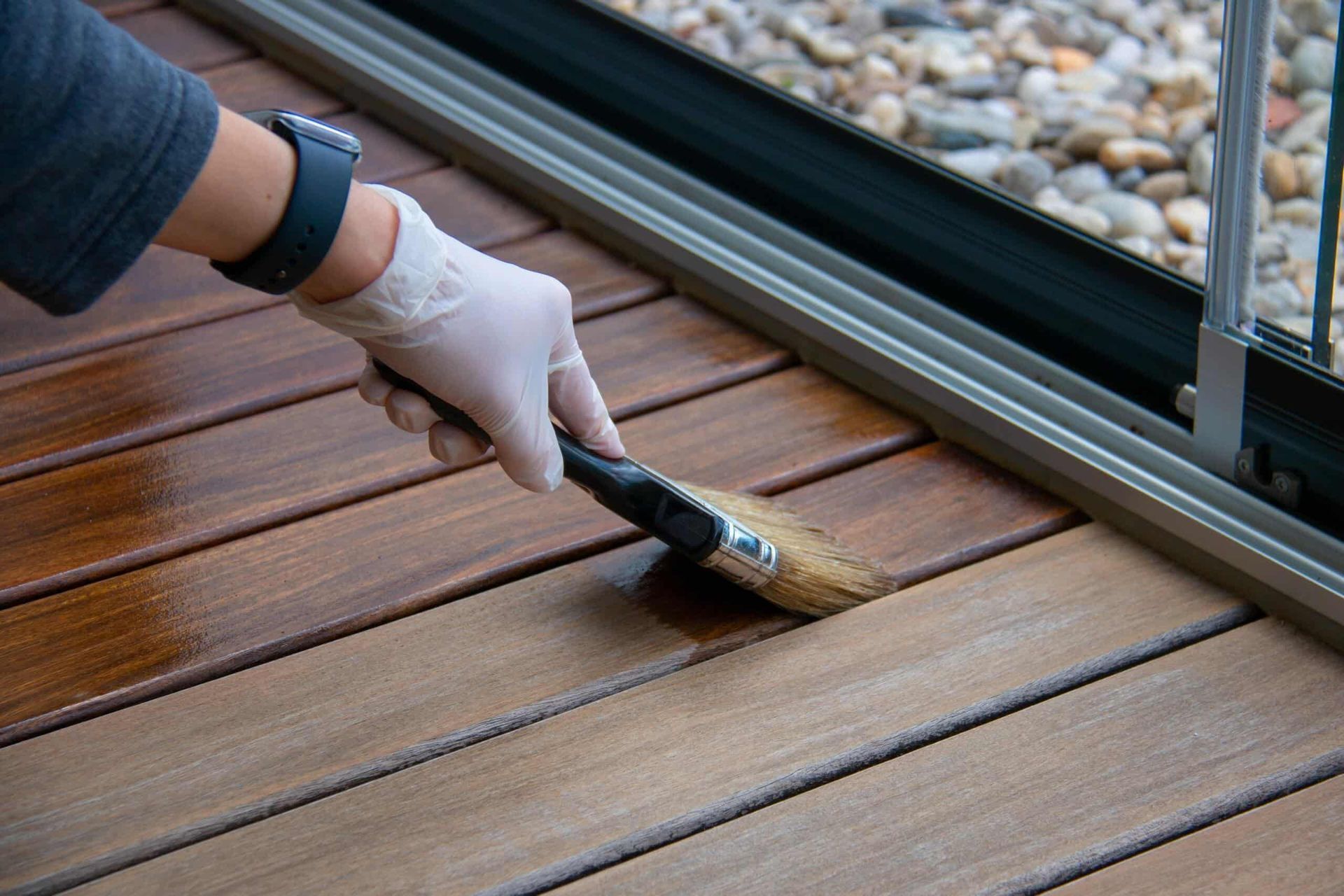 A Person is Painting a Wooden Deck With a Brush — NHM Painting & Projects in Ciccone, NT