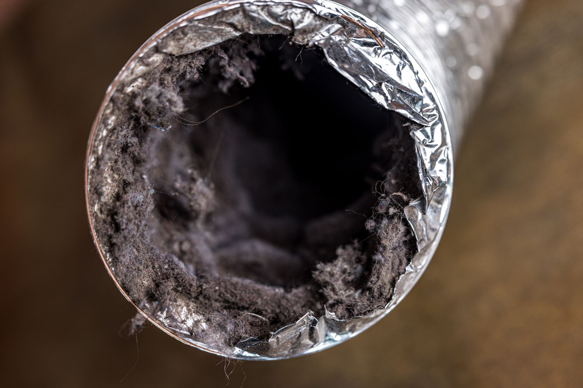 close-up view inside a flexible aluminum air duct clogged with thick dust and debris.
