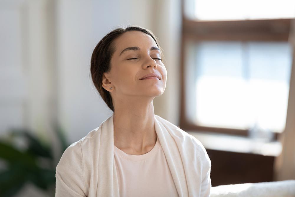Content woman sitting on sofa with closed eyes breathing air cleaned by Duct Cleaning Specialists at