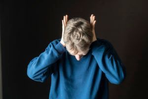 A man in a blue sweater is covering his ears with his hands.