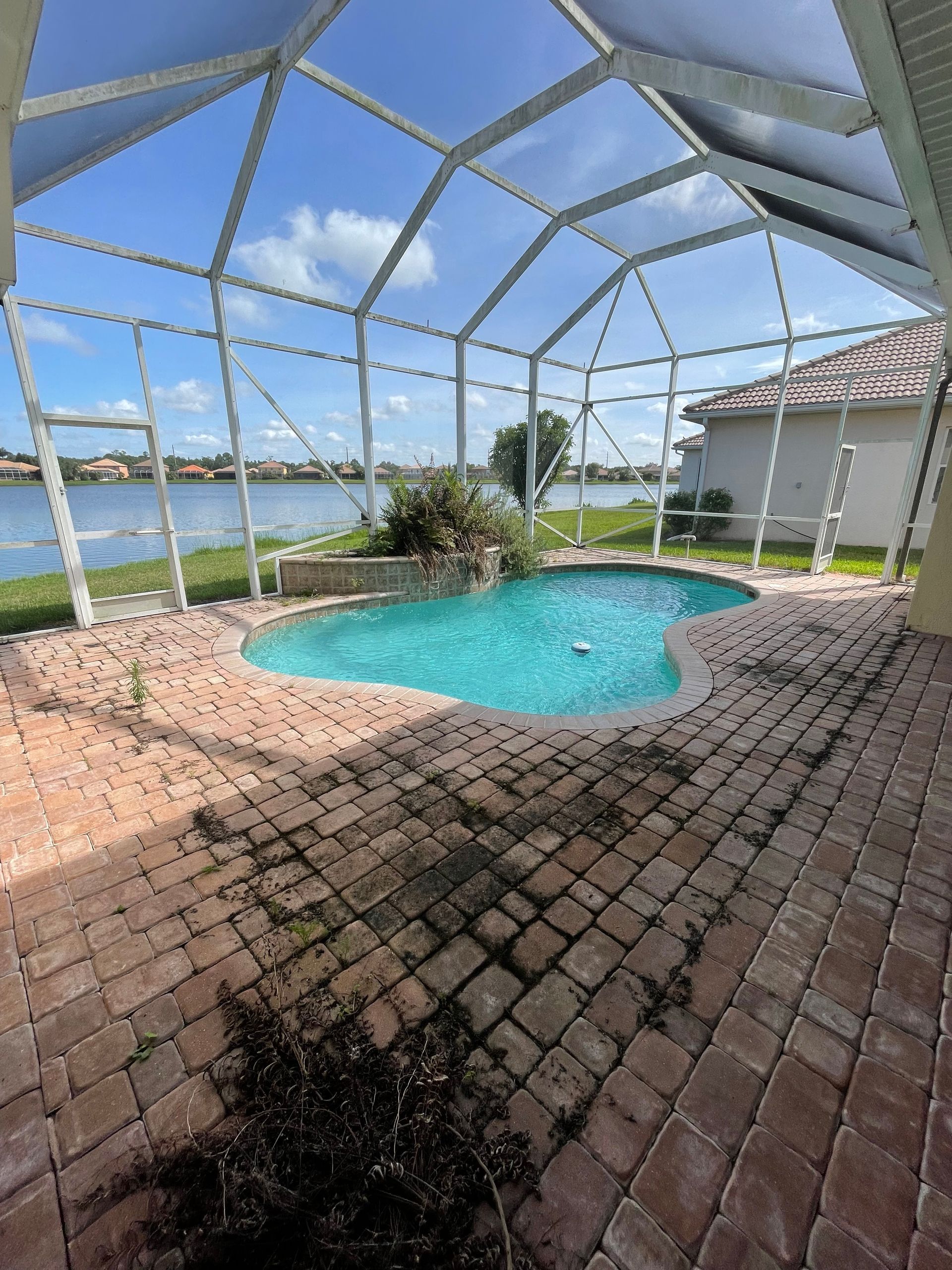 Screened-in patio with a small turquoise pool, paver floor, and lake view under a bright sky