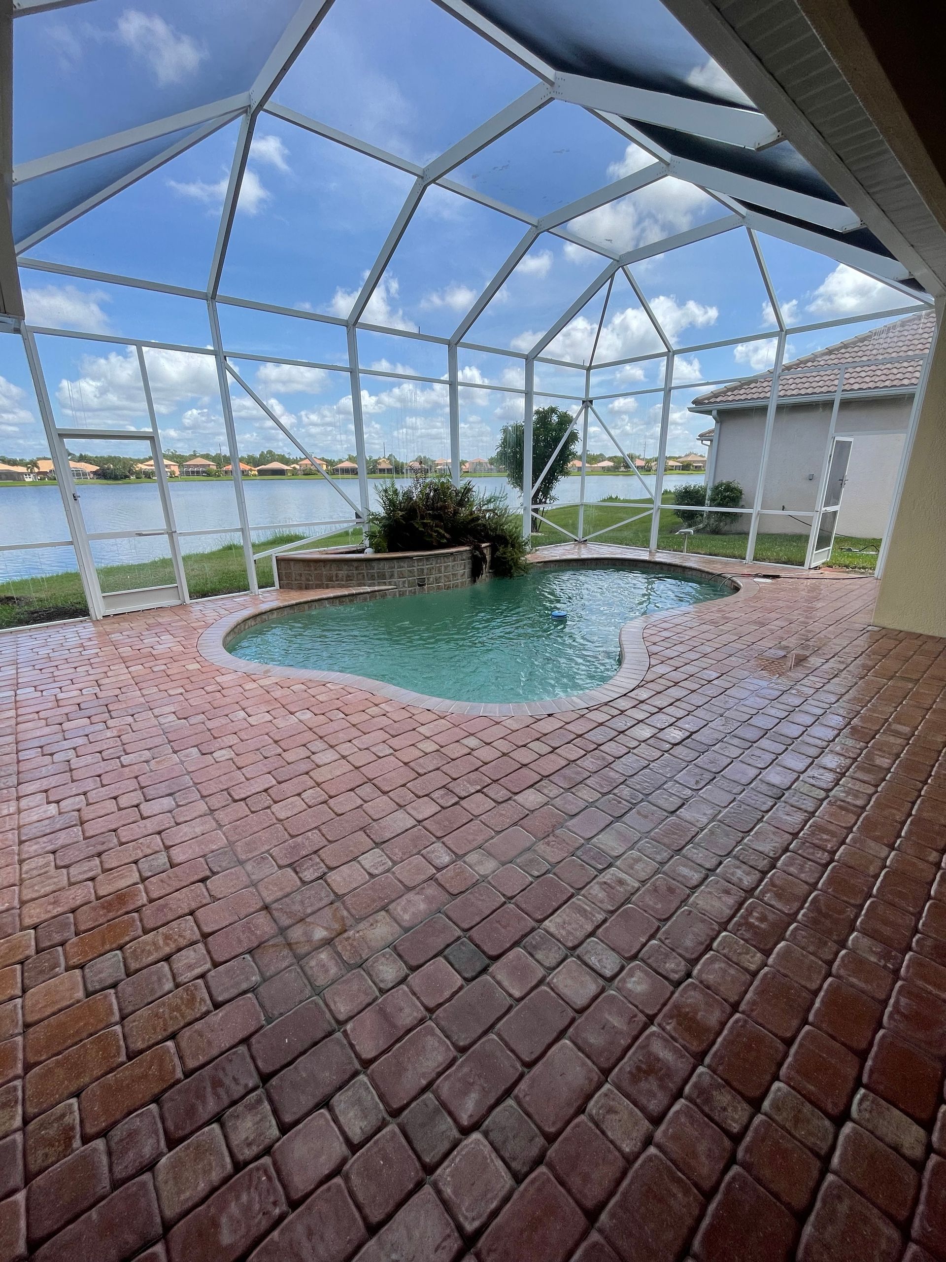 Screened patio with a small pool, brick floor, and lake view under a blue sky