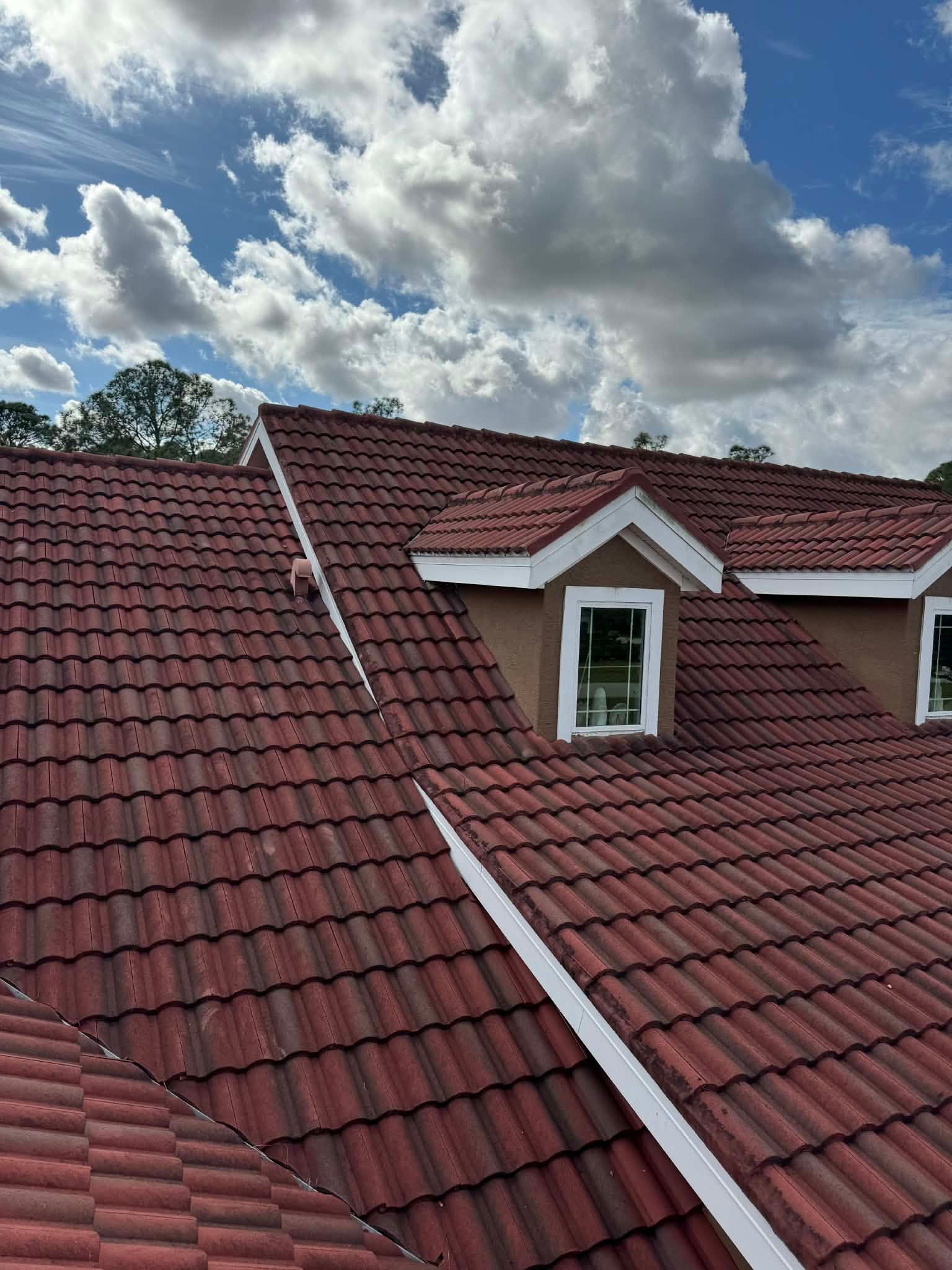 Red-tiled roof with two dormer windows under a cloudy blue sky