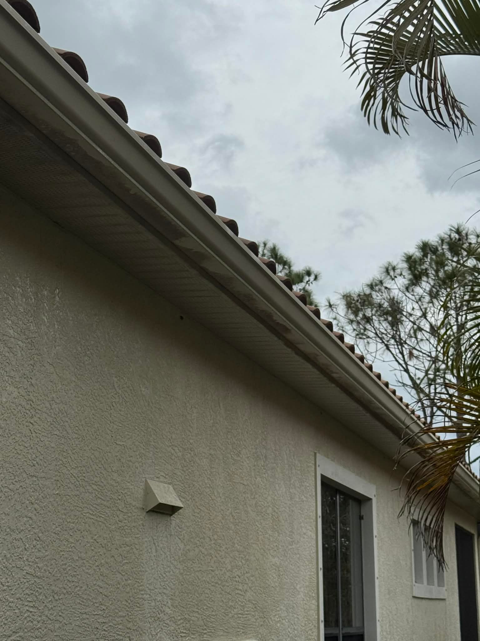 Exterior of a stucco house with a tiled roof, window, and overcast sky above.