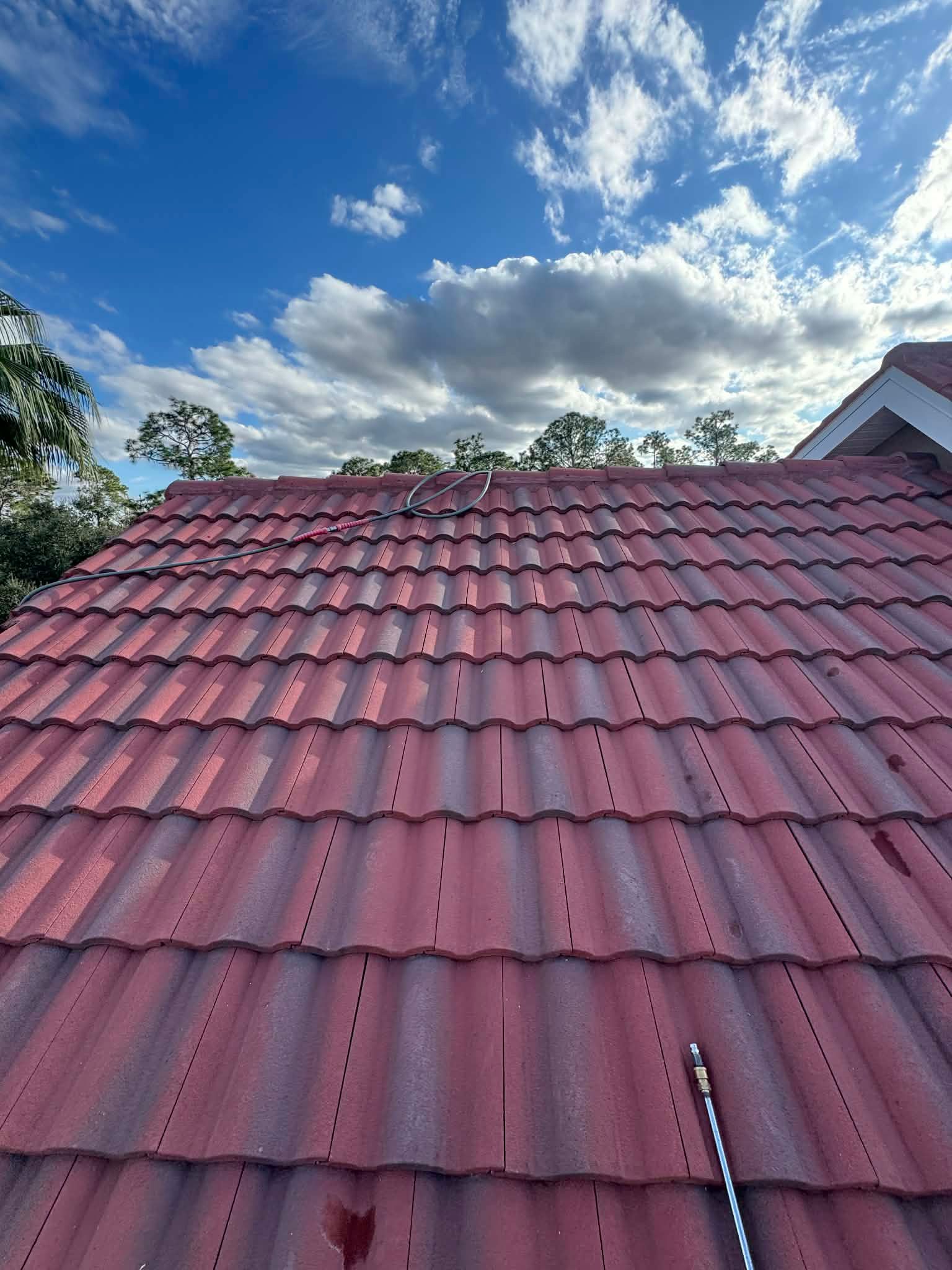Red tiled roof under a blue sky with scattered clouds and trees in the background