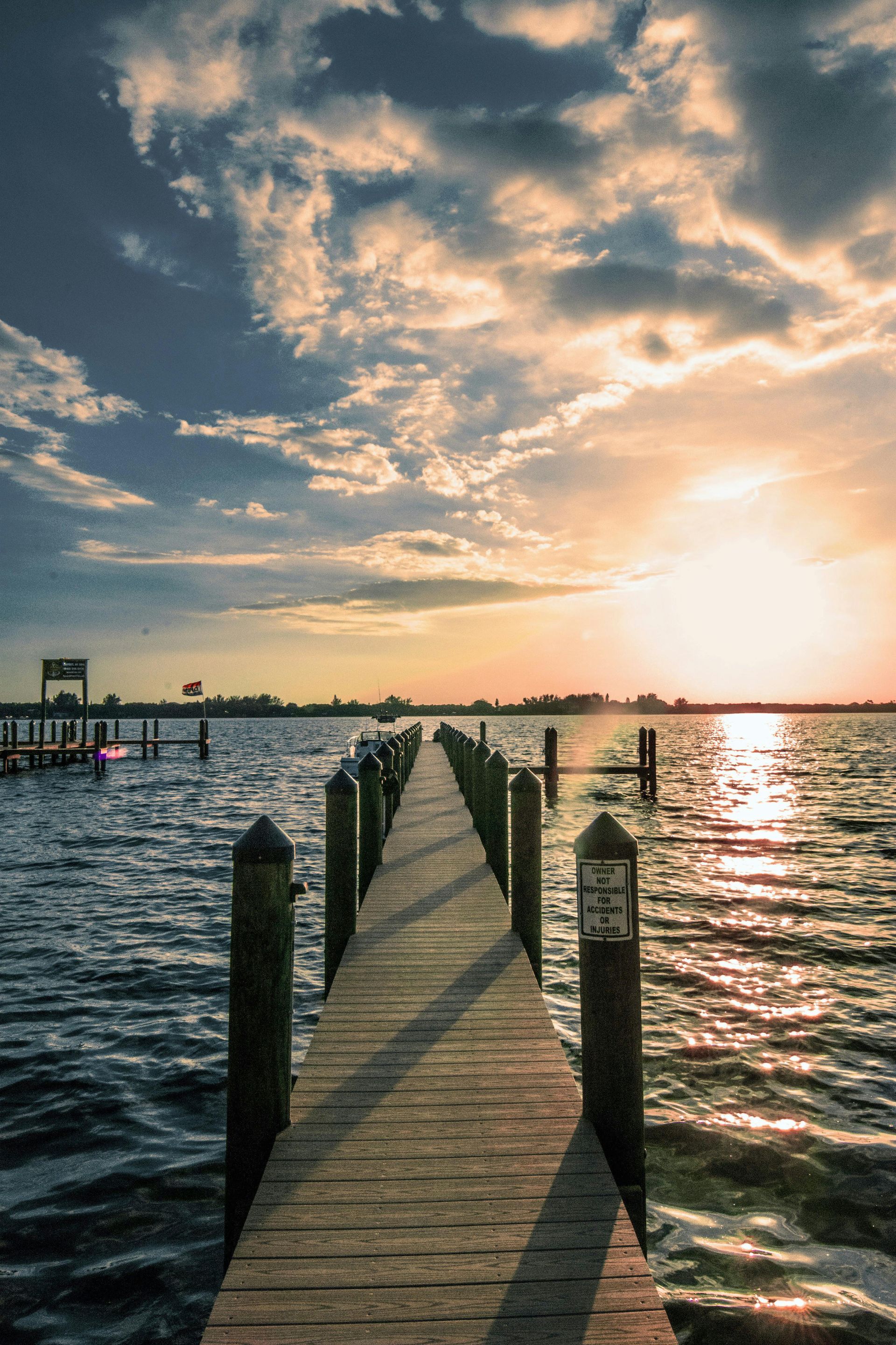 Wooden pier leading into a sunlit ocean at sunset with a dramatic cloudy sky