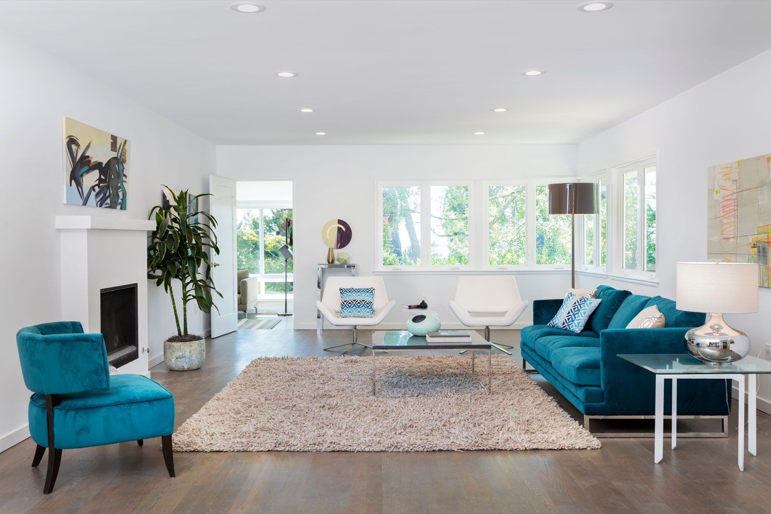 Bright modern living room with teal sofas, shag rug, fireplace, and large windows
