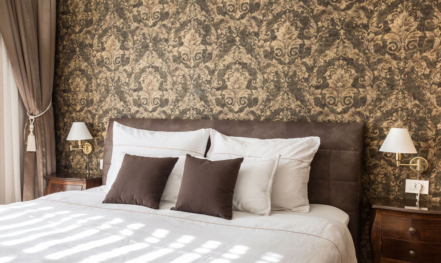 Elegant bedroom with a tufted brown headboard, patterned wallpaper, white bedding, and bedside lamps