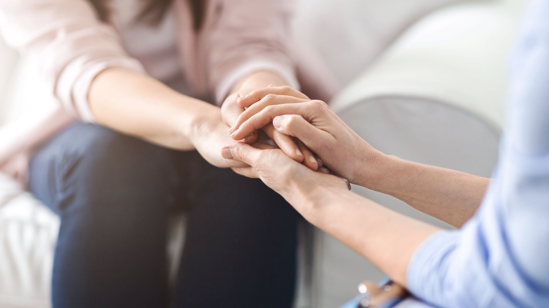 A woman is holding another woman's hand while sitting on a couch.