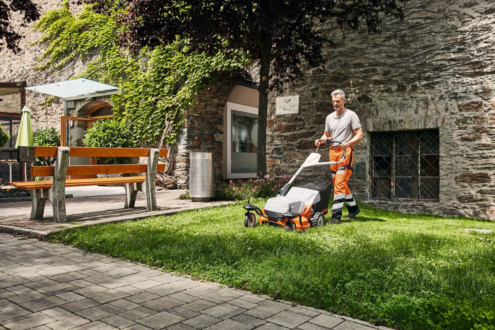 Jardinier coupant l'herbe d'un  jardin avec une tondeuse Stihl