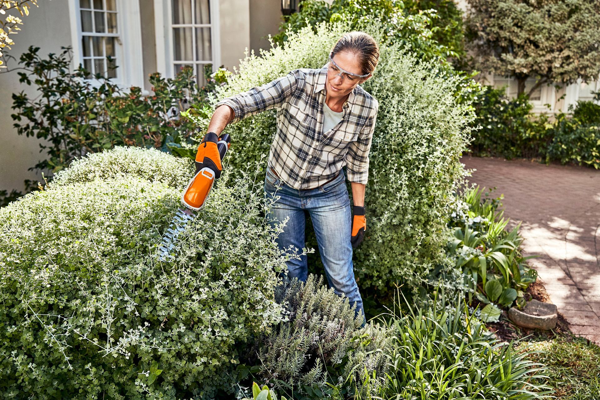 Jeune femme utilisant un taille-haie Stihl pour couper ses buissons