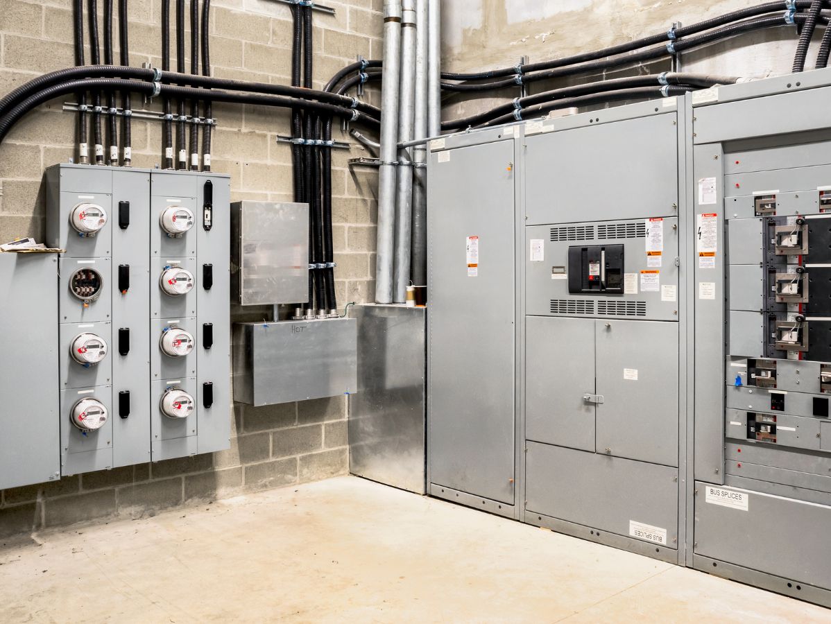 Electrical equipment room with gray metal panels, wires, meters, and brick walls.