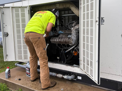 Electrician in gloves tests wiring with a multimeter inside an electrical panel.