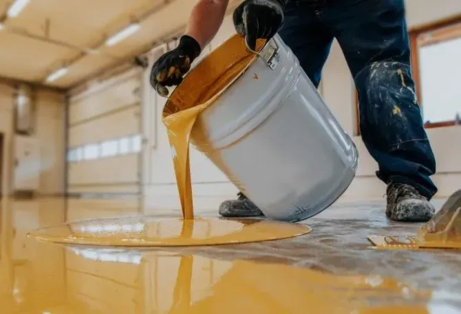 Worker pouring liquid gold-colored epoxy onto a floor.