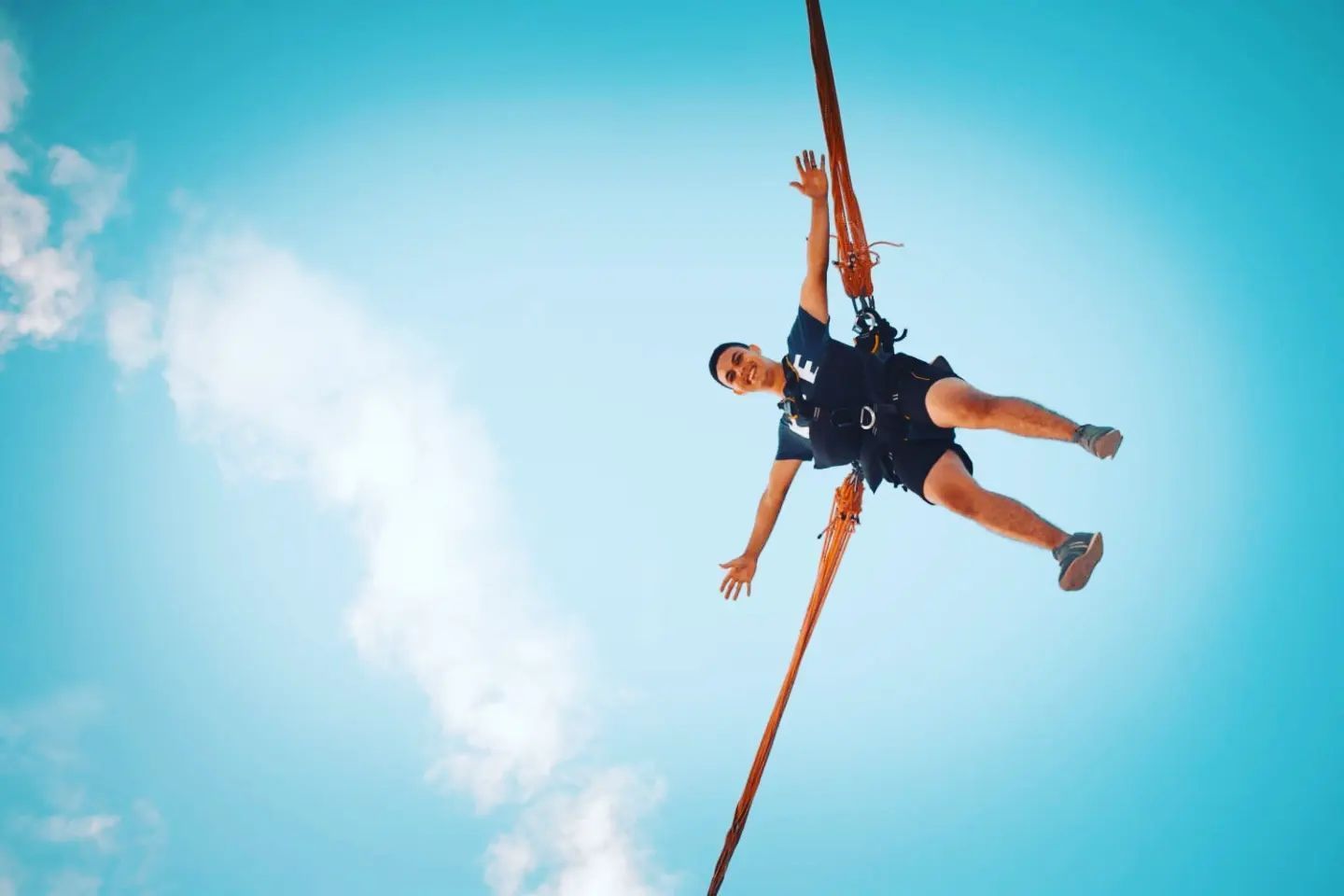 Persona suspendida en el aire con cuerdas, sonriendo. Fondo de cielo azul brillante.