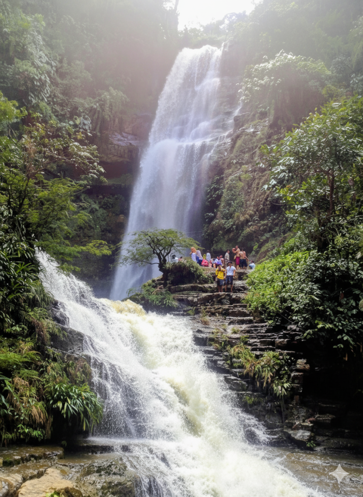 Cascada cayendo sobre rocas; varias personas se encuentran cerca del centro. Un follaje verde rodea la cascada.