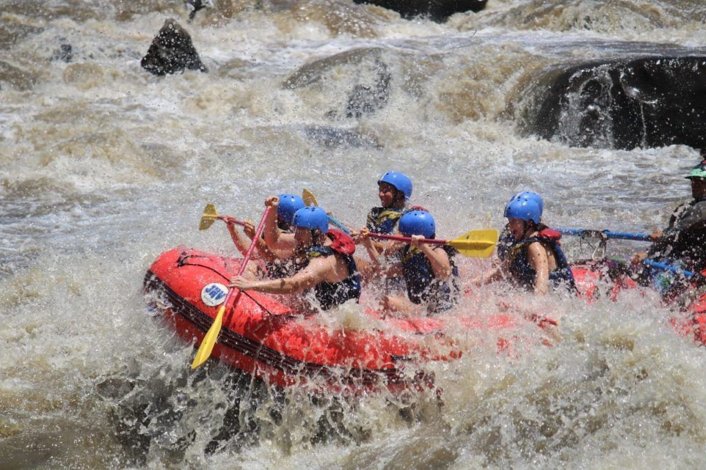 Los rafters en una balsa roja navegan por rápidos de aguas bravas, con los remos en alto, usando cascos