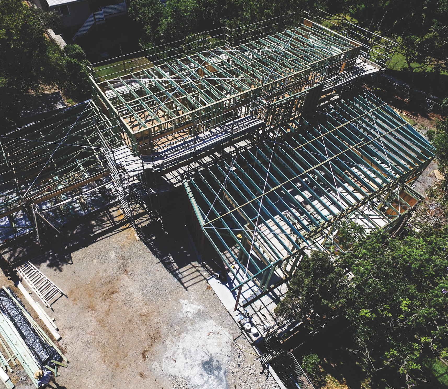 Aerial view of a brown shingled house roof with solar panels and surrounding trees