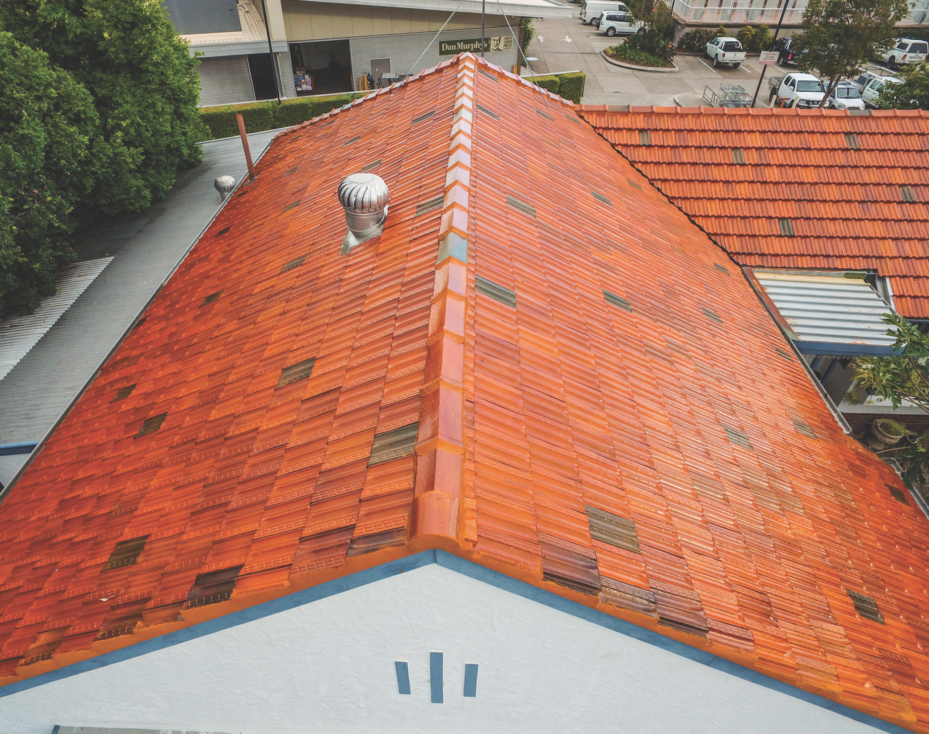 Aerial view of a red-tiled roof with a chimney and blue-trimmed facade below