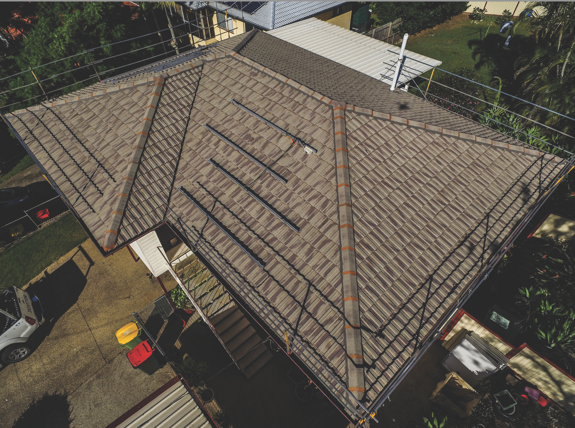 Aerial view of a brown shingled house roof with solar panels and surrounding trees