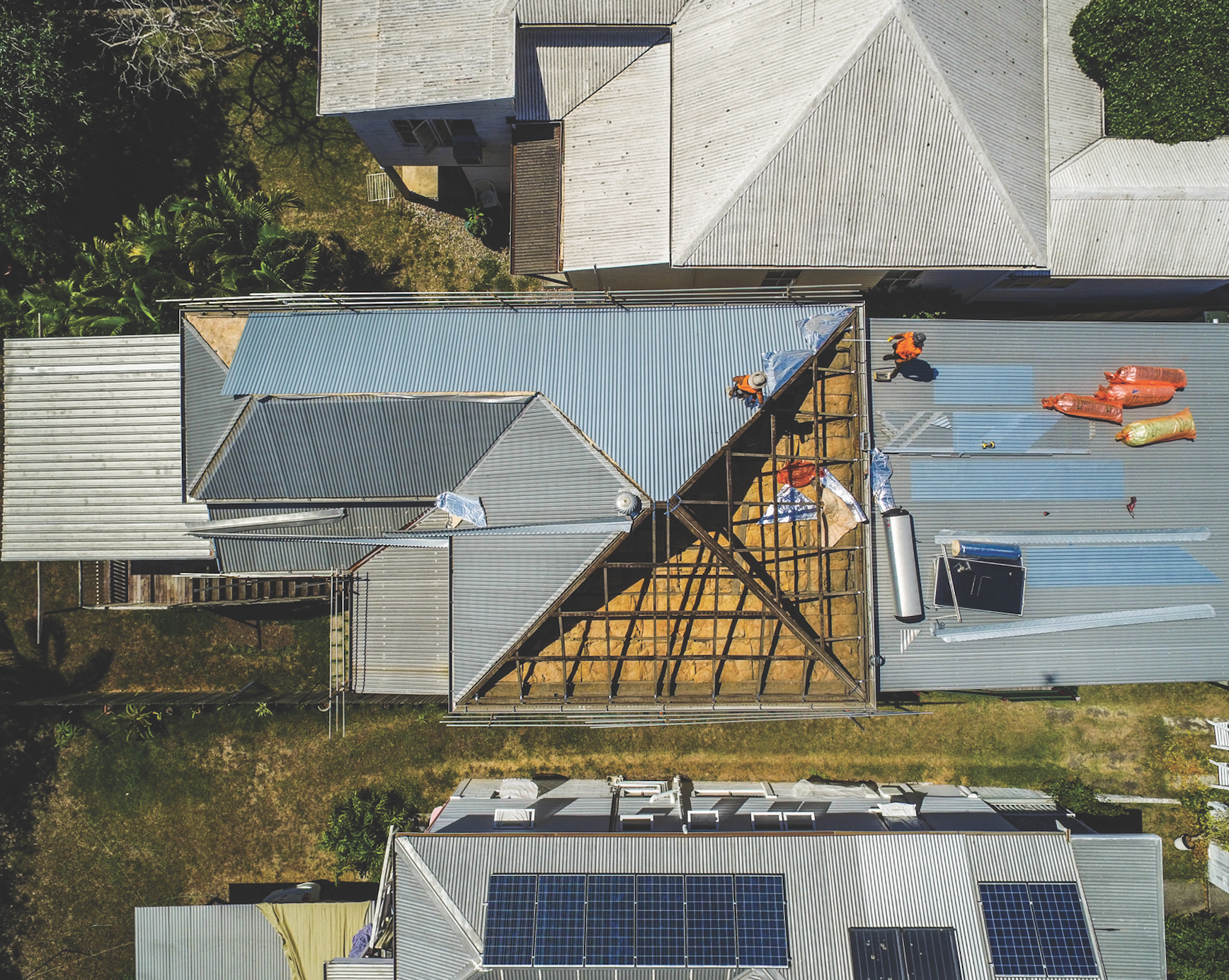 Aerial view of a roof being repaired, with workers on blue metal roofing panels and scattered tools.