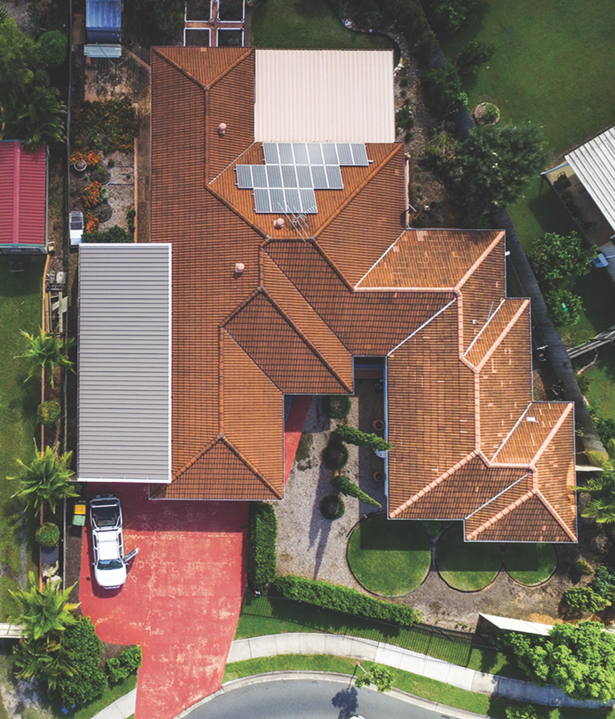 Aerial view of a brown shingled house roof with solar panels and surrounding trees