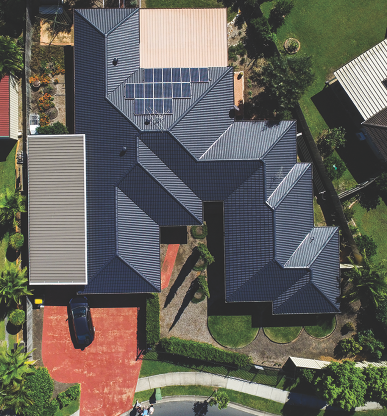 Aerial view of a house with a red roof and rooftop solar panels.