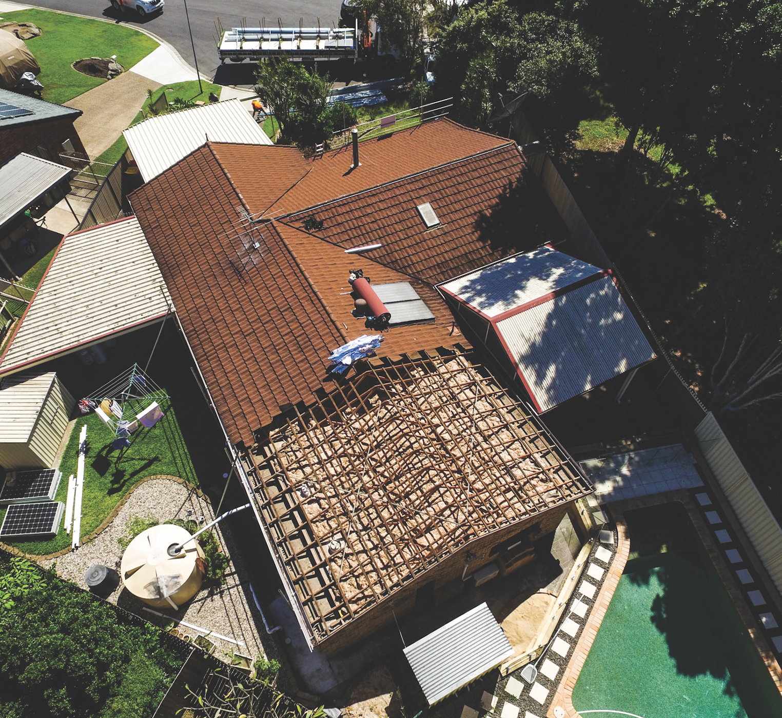 Aerial view of a house with red roof, workers repairing a section, and a swimming pool beside it