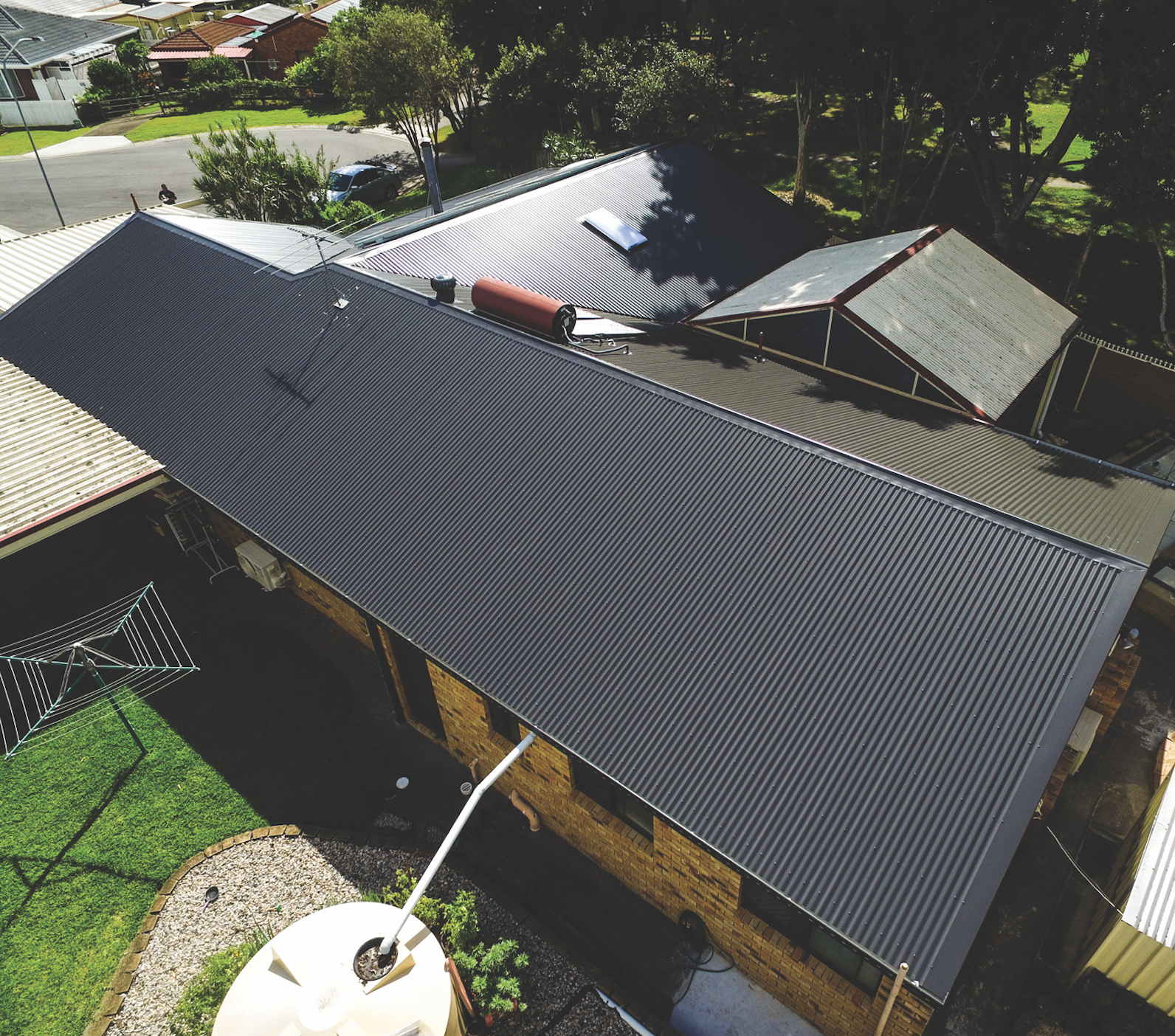 Aerial view of a house with a dark metal roof and surrounding trees and yard.