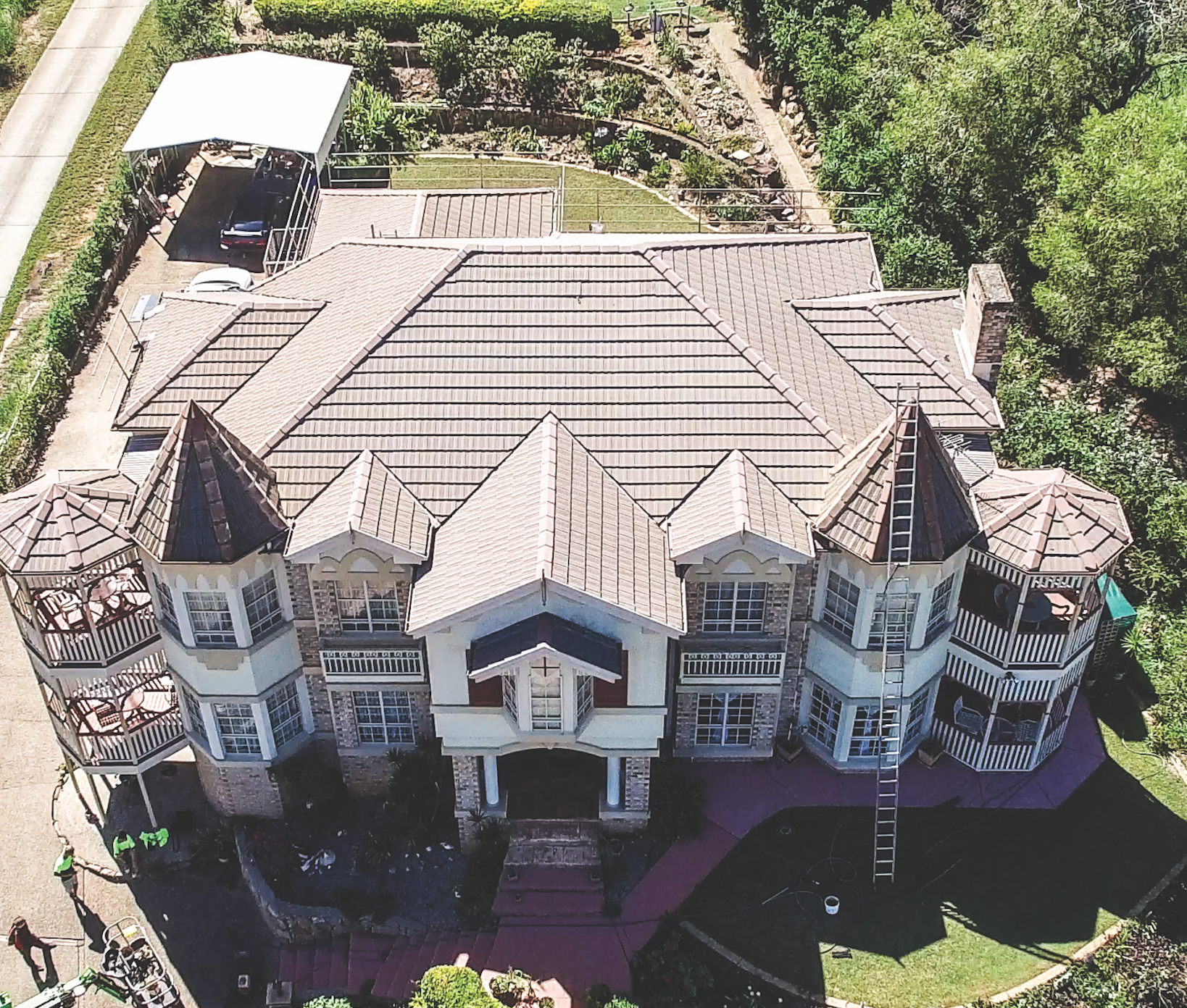 Aerial view of a large castle-like mansion with turrets and a gray roof, surrounded by trees.