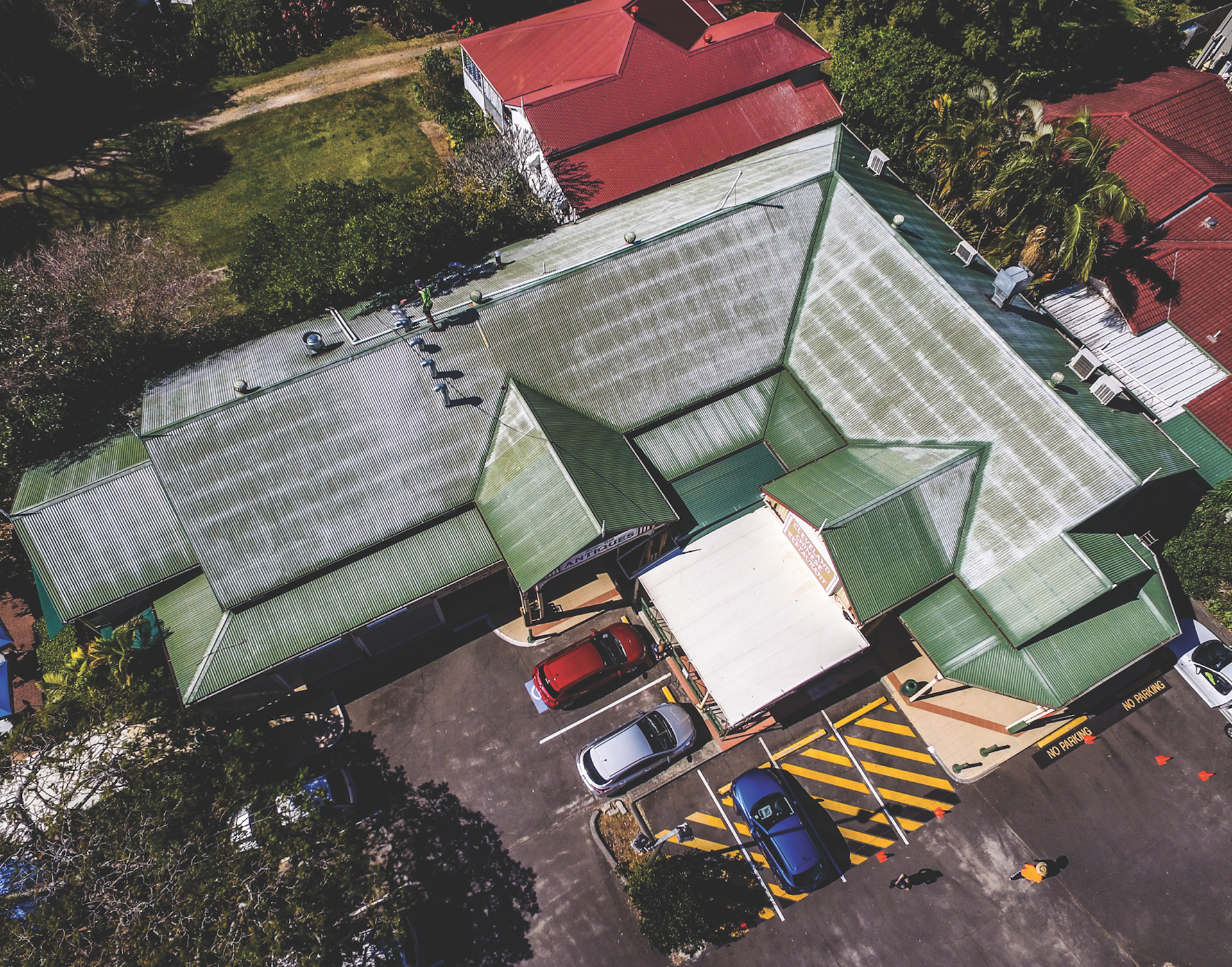 Aerial view of a brown shingled house roof with solar panels and surrounding trees