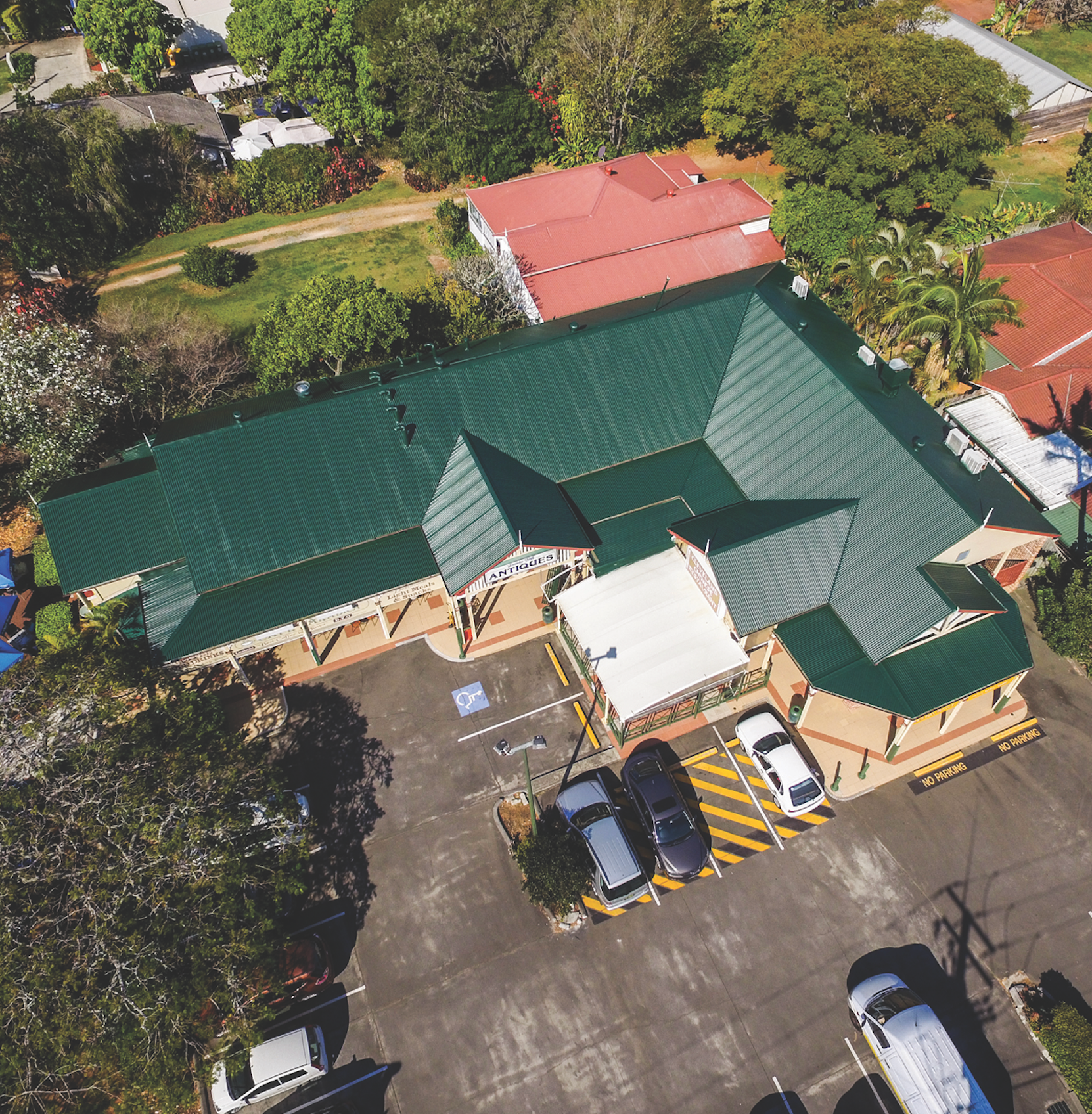 Aerial view of a green-roofed building with parked cars and surrounding trees and pavement.