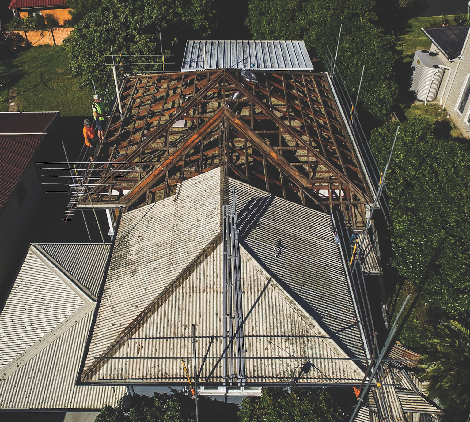 Aerial view of a house roof under construction, with exposed wooden trusses and gray shingles.
