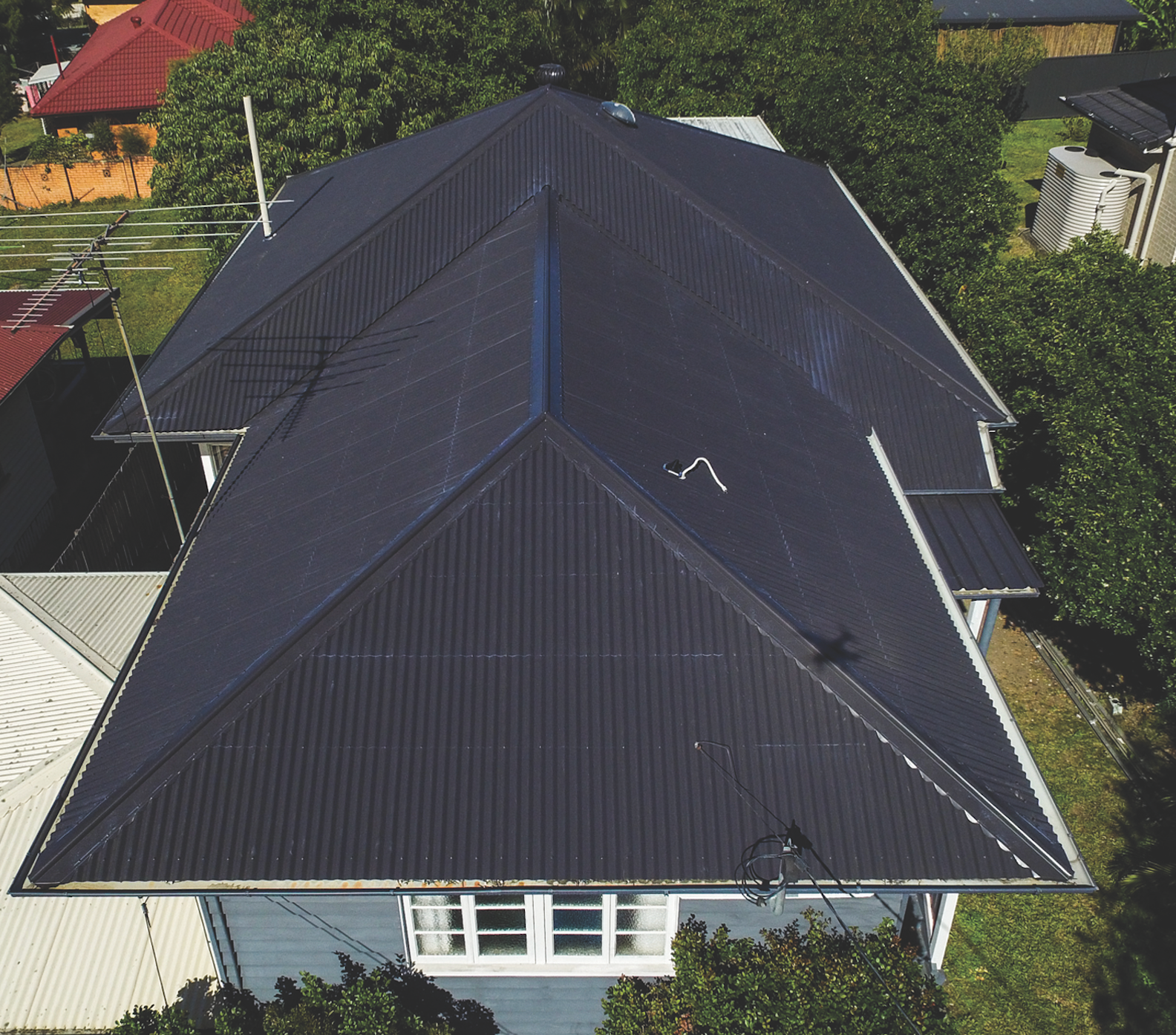 Aerial view of a dark gray roof on a house surrounded by trees and neighboring homes.