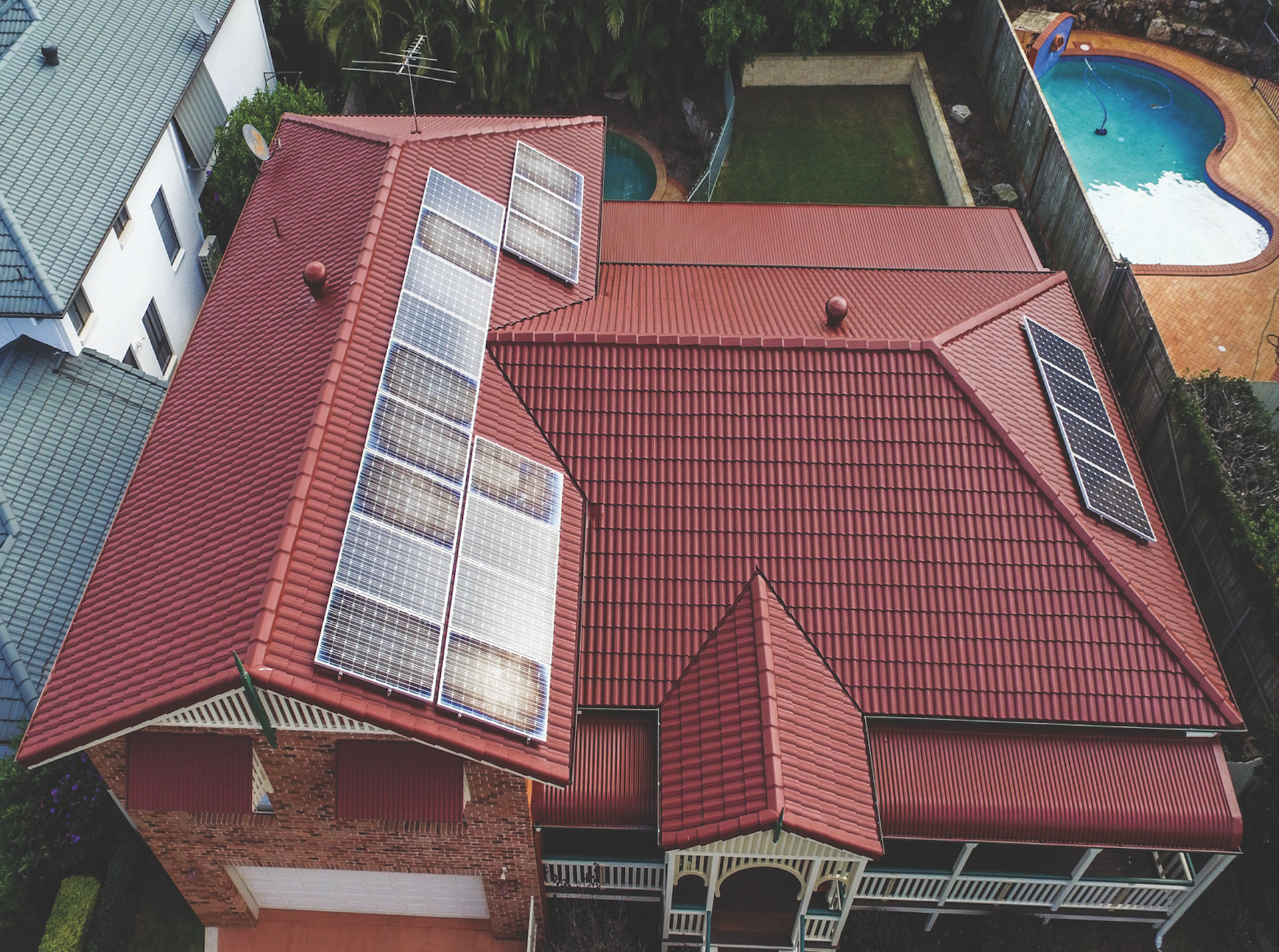 Aerial view of a house with a red tile roof, skylights, and a swimming pool in the backyard