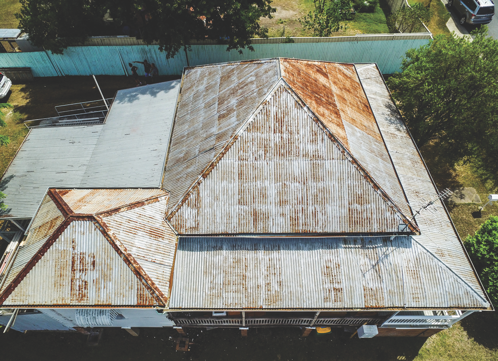 Aerial view of a weathered corrugated metal roof with rust patches and a small attached section.